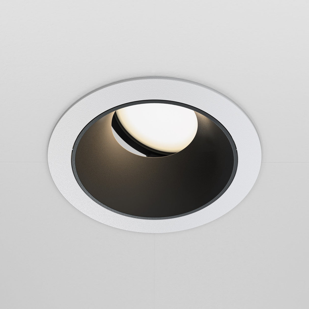 The Share Round Recessed Swivel Downlight features a circular, white frame and a partially visible light inside its black interior, enhancing modern interiors with an even glow across smooth, light-colored ceilings.