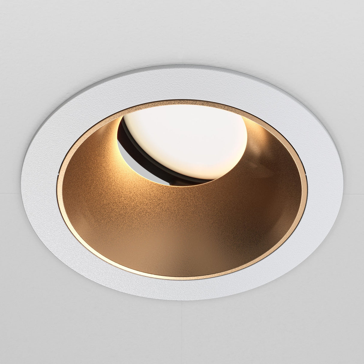 A close-up of the Share Round Recessed Swivel Downlight showcases its modern design, featuring a circular matte gold interior with a white outer ring. The adjustable light partially reveals the source, casting a warm glow within the fixture.