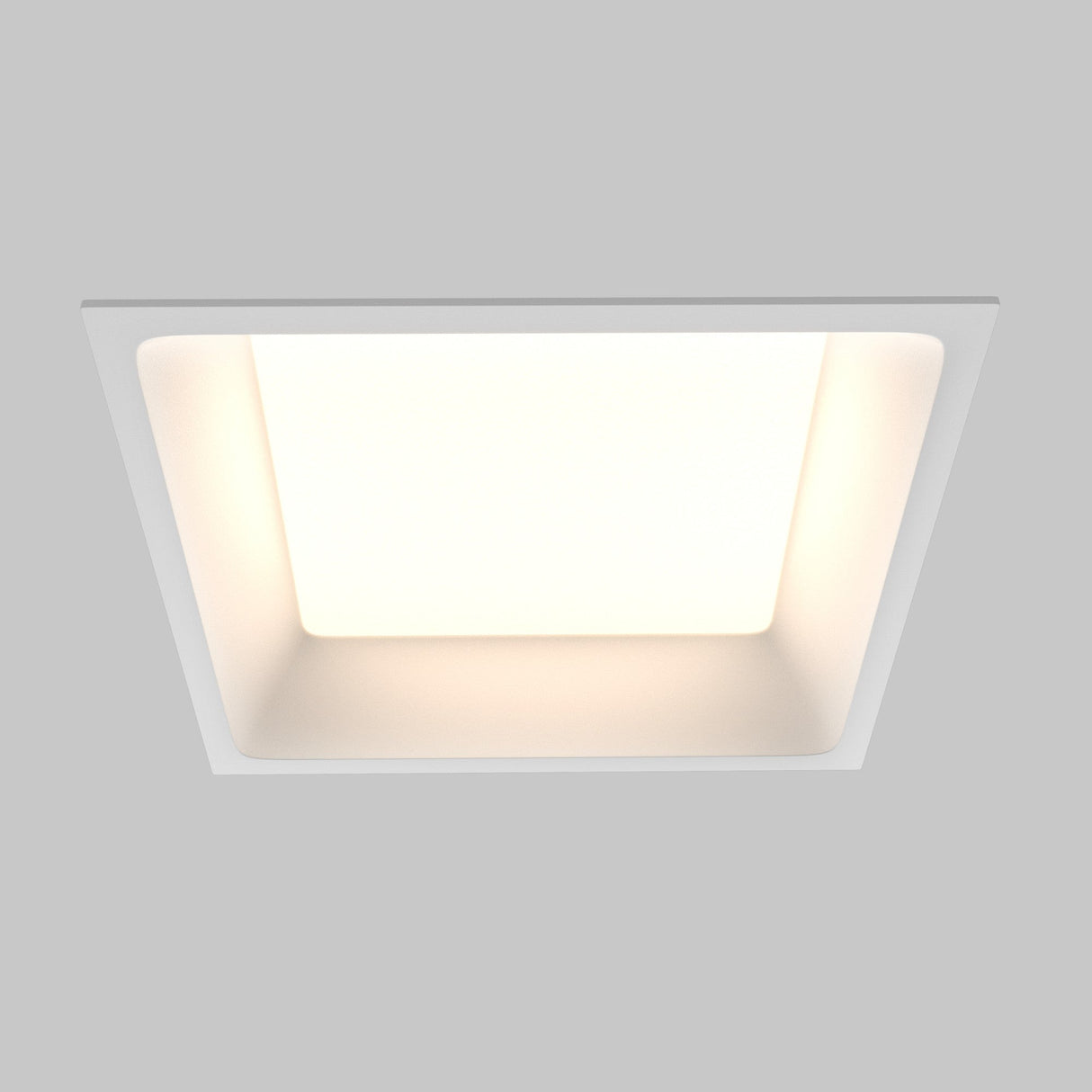 The Okno CCT LED Square Recessed Downlight 18W (3000-6000K) in white emits a soft glow on a plain gray background, highlighting its energy efficiency and adjustable color temperature for versatile ambiance.
