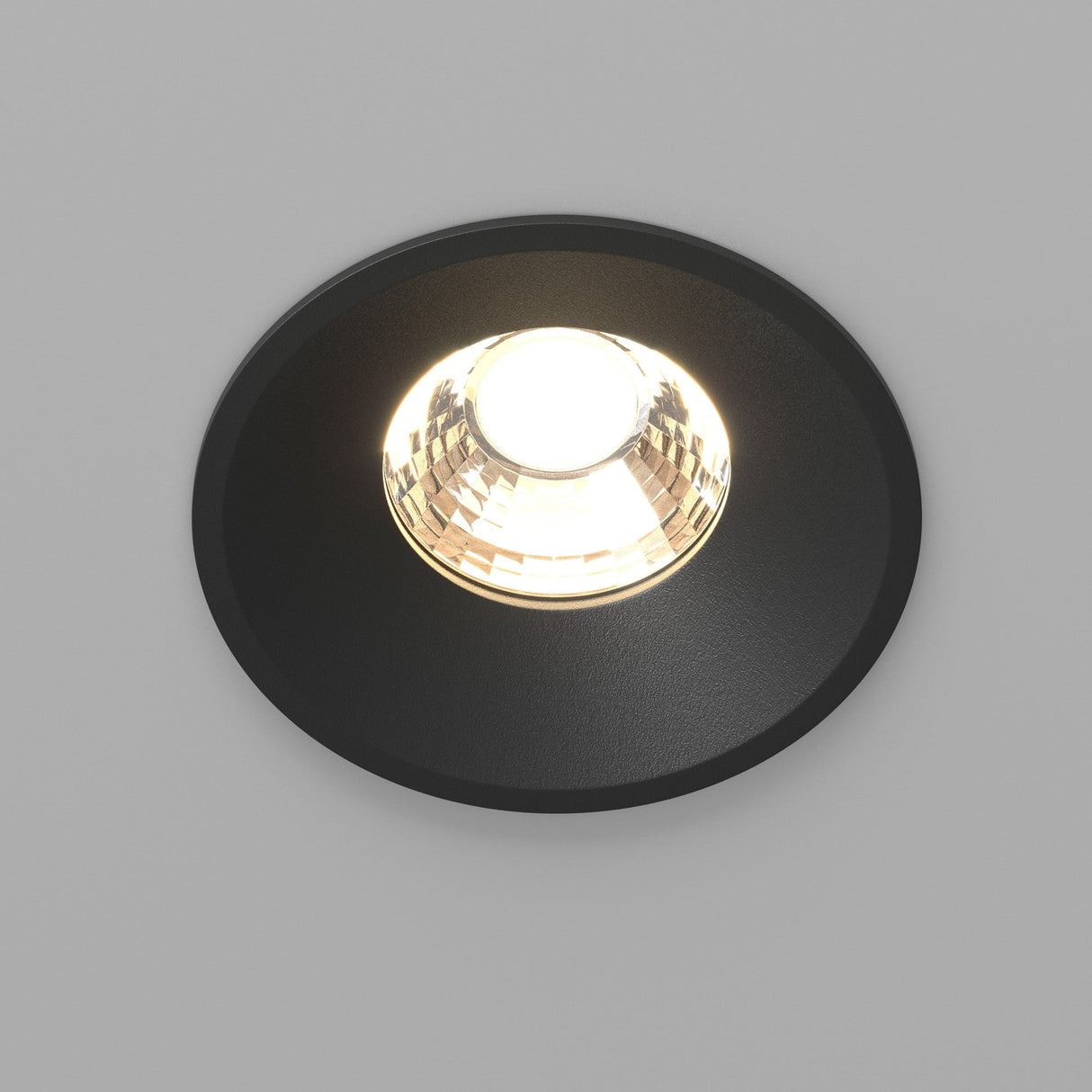 The Round LED Recessed Downlight 12W 3000K - Black is shown lit against a plain white background, casting a bright, focused beam. Its matte black finish and reflective interior give it a sleek, minimalist appearance.