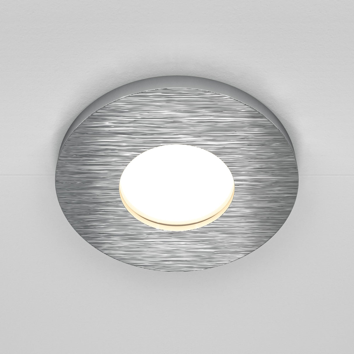 The Stark Fixed Round Recessed Downlight in silver features a modern brushed metal frame with a glowing center, perfectly mounted on a white ceiling. Its compatible with GU10 bulbs for versatile lighting options.
