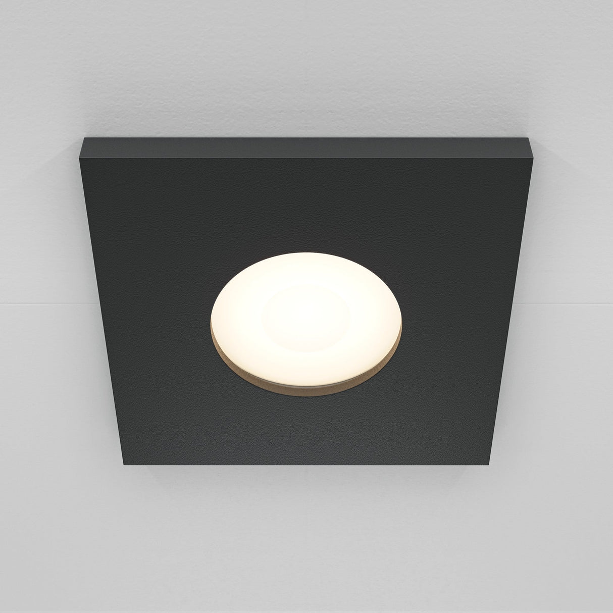 The Stark Fixed Square Recessed Downlight - Black has a central white circular bulb, is IP65-rated, and offers a modern look on a white ceiling, casting subtle shadows.