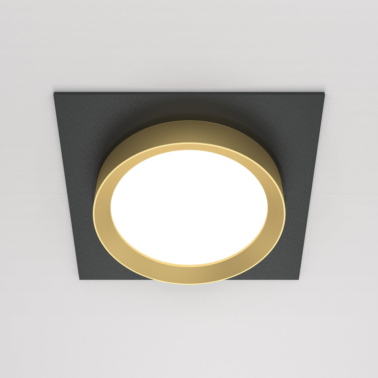The Hoop Single Fixed Square Recessed Downlight boasts a sleek LED design with a circular illuminated center surrounded by a golden ring, elegantly contrasting against its black and gold theme, all mounted on a square dark background.