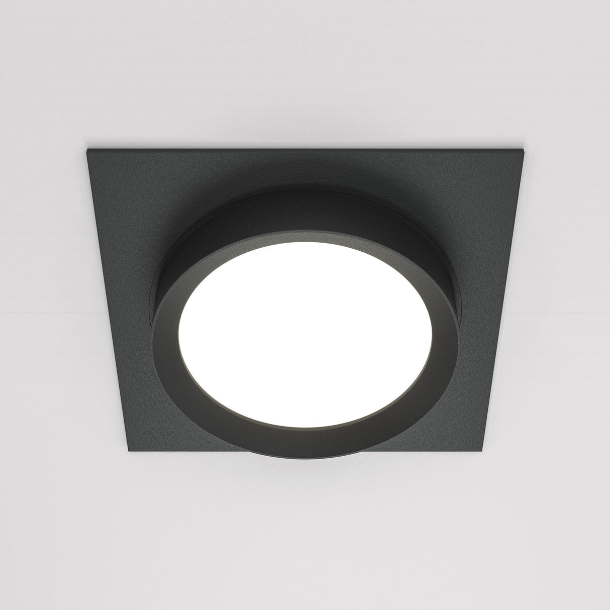 The Hoop Single Fixed Square Recessed Downlight in black features a round, illuminated center that provides energy-efficient LED lighting. Its modern, minimalist design looks elegant against a white ceiling.