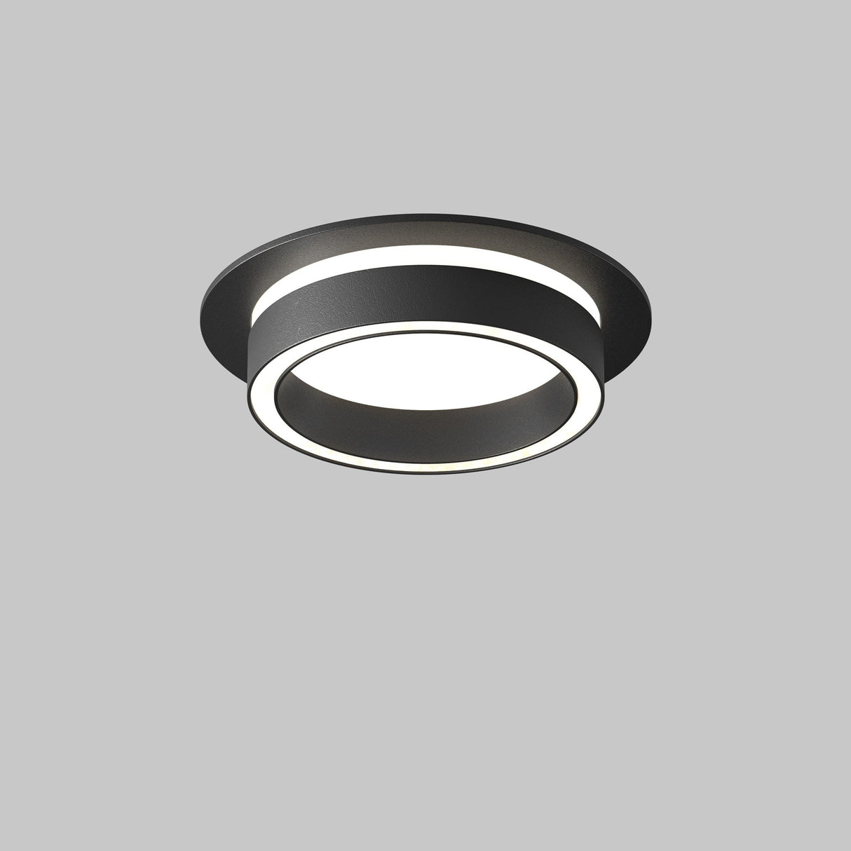 The Orlo Fixed Round Recessed Downlight - Black is a modern ceiling fixture with a matte black outer ring and glowing inner ring, emitting bright white light against a plain gray background, making it ideal for industrial decor.
