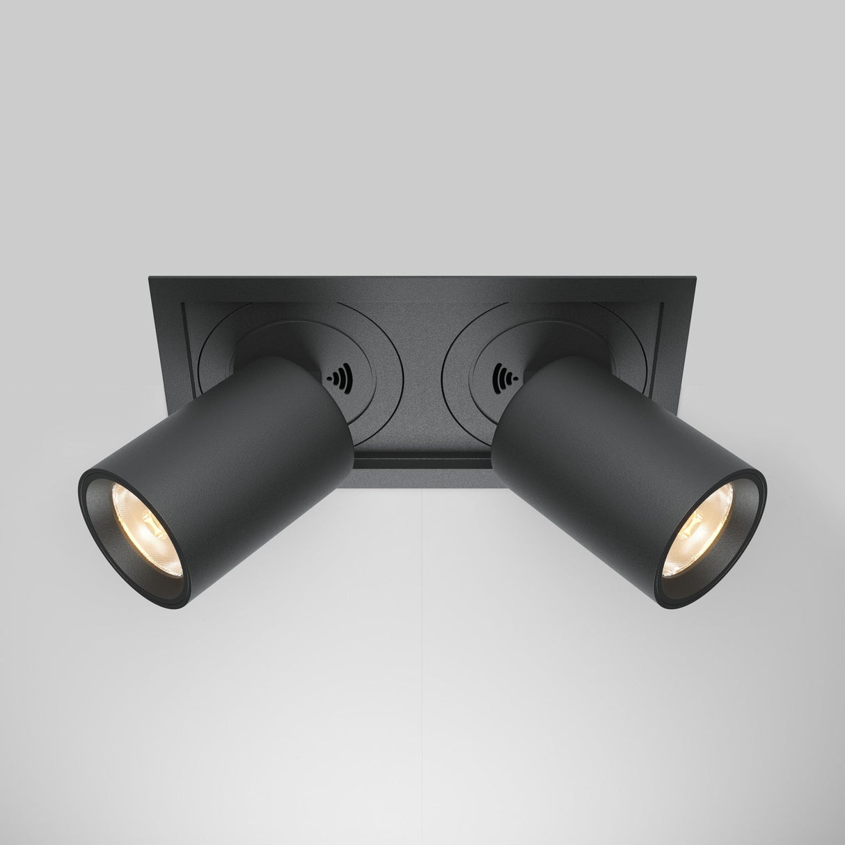 The Hidden Twin Adjustable Retractable In-Out LED Rectangular Recessed Downlight in black features energy-efficient LED technology. Each cylindrical spotlight contains a warm white bulb and is mounted on a rectangular base against a gray background.