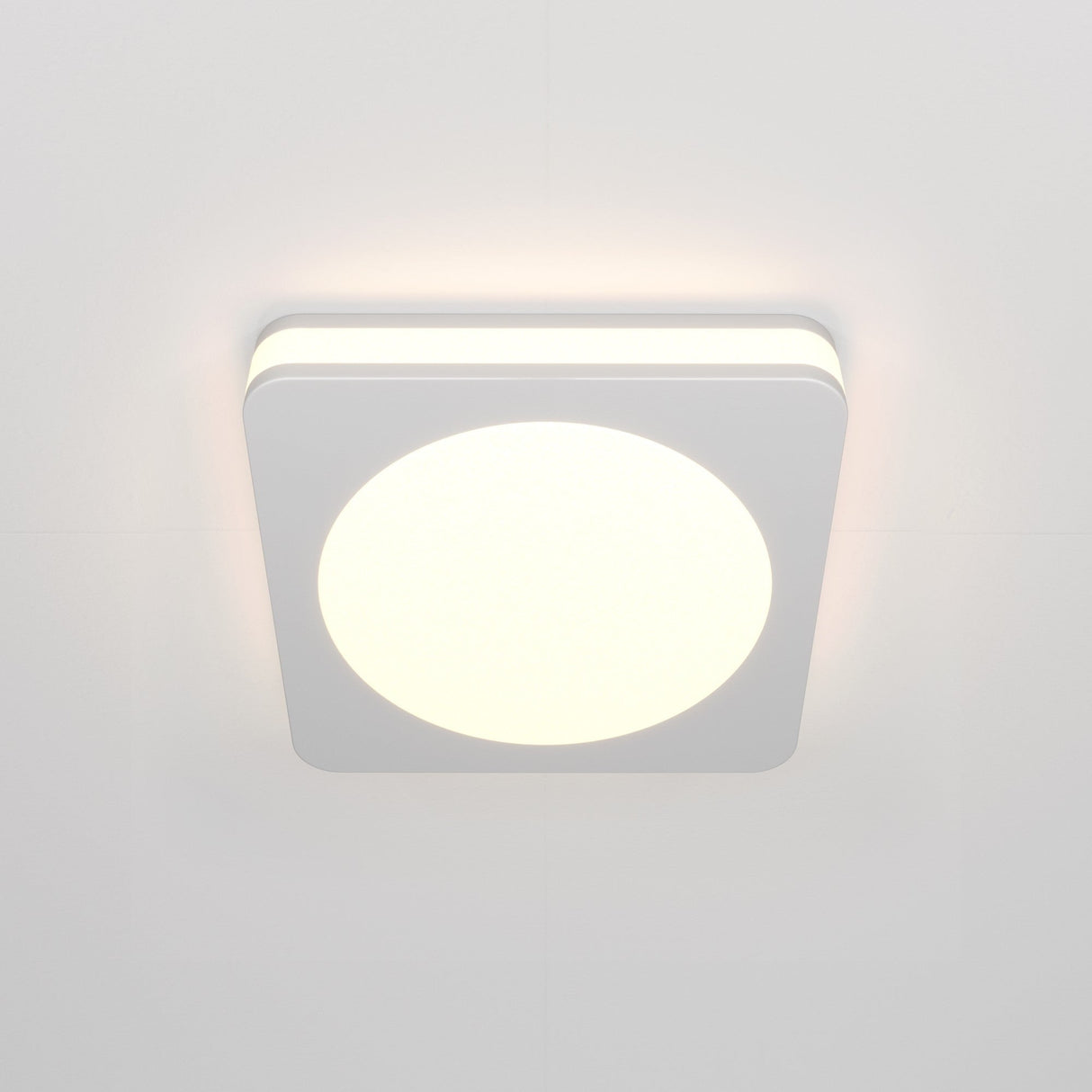 The Phanton LED Recessed Downlight 7W 3000K - White is a square ceiling light fixture with rounded corners, featuring a bright circular center. It uses energy-efficient LED technology and is mounted on a pale ceiling.