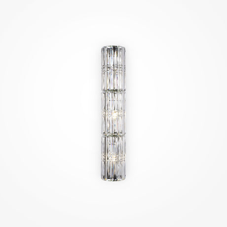 The Facet 3 Light Long Wall Light in chrome is a vertical cylindrical glass sconce with crystal and faceted panel detailing, emitting a soft, diffused light. Mounted on a plain white wall, it adds an elegant and modern touch to any space.