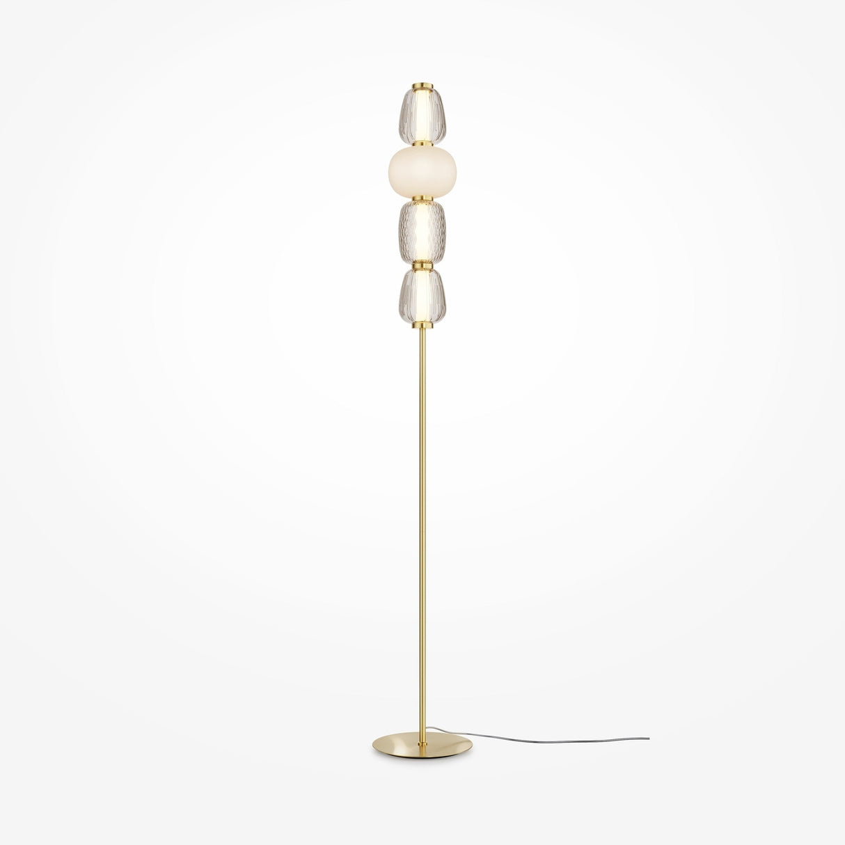 The Pattern LED Floor Lamp - Gold is tall and modern with a slim gold base and pole, featuring four stacked textured glass orbs in clear and frosted finishes. Its black power cord enhances energy efficiency against a plain white backdrop.