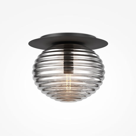 The Reels Ceiling Light features a ribbed smoked glass globe with a visible bulb, elegantly mounted on a circular black metal base. Its turned off, highlighting the globes reflective surface against a plain white background.