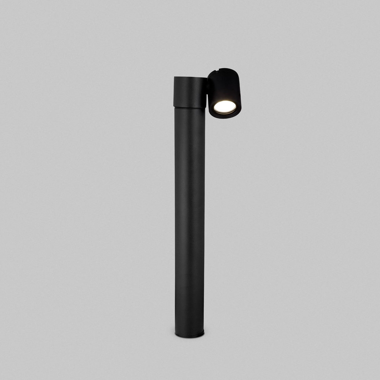 The Wall Street 1 Light Bollard 55cm in black features a modern cylindrical base and adjustable spotlight head, standing elegantly against a plain grey background.