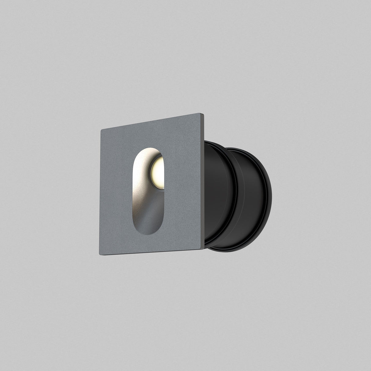 The Via Urbana Outdoor LED Recessed Wall Light features a minimalistic design with a square gray faceplate, circular black housing, and a small recessed oval opening. It has corrosion-resistant construction, an IP54 rating, and emits light against a plain gray background.