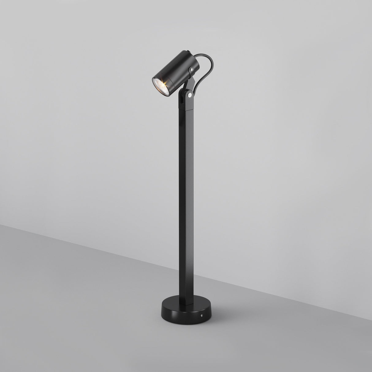 The Scope Bollard Light, a sleek black floor lamp with a cylindrical head, is mounted on a tall narrow pole with a round base, emitting a soft glow against the minimalist gray background.