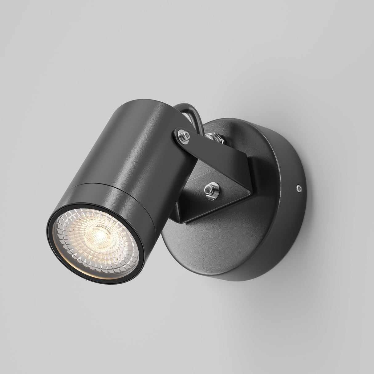 The Scope Outdoor Wall Light - Black is a modern cylindrical wall-mounted spotlight with an adjustable bracket. It emits a warm glow and is attached to a round base on a plain light gray wall, offering durable exterior lighting.