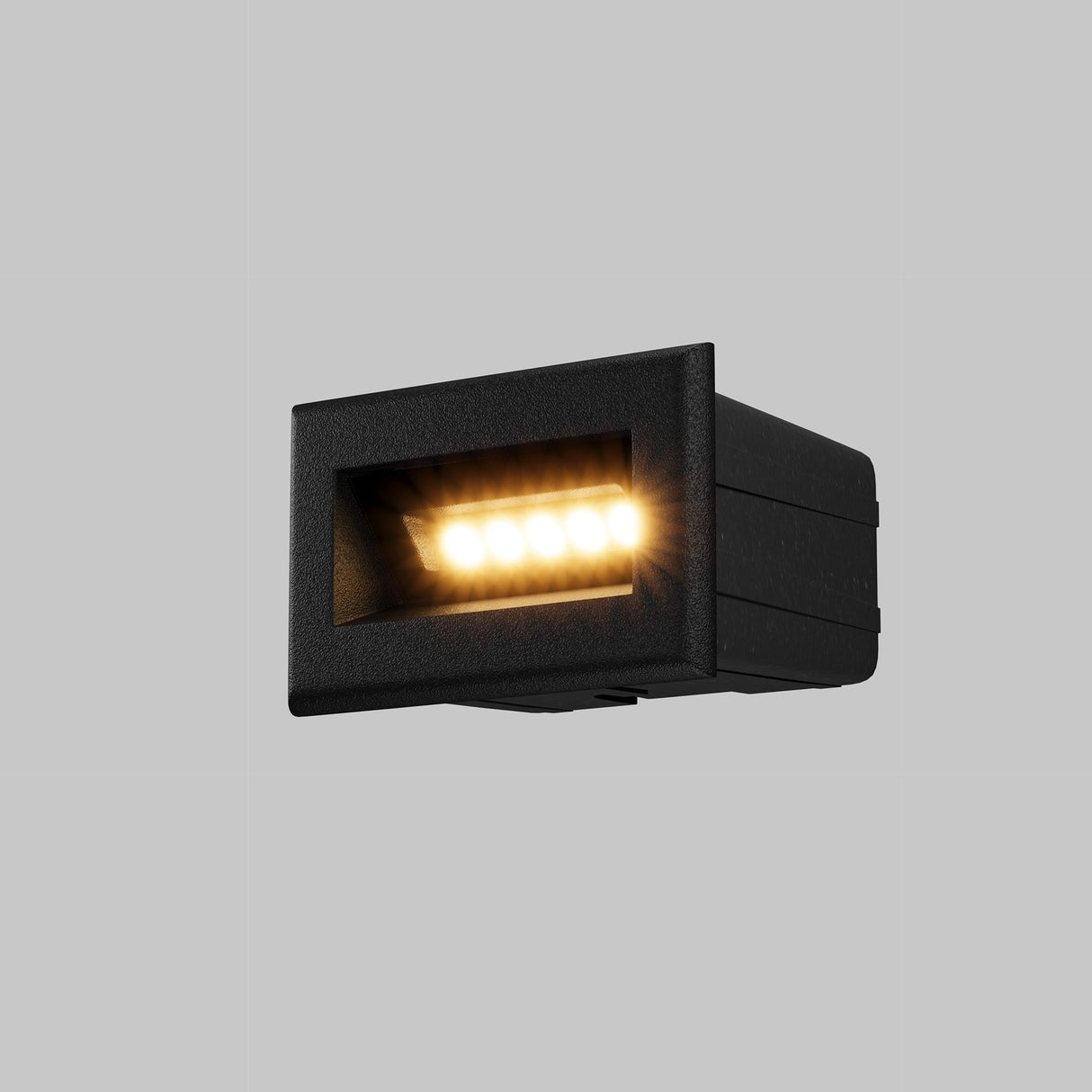 The Bosca Outdoor LED Recessed Wall Light in black features a grid design and emits a warm, soft glow against gray backgrounds. It focuses light downward for outdoor use and is IP65-rated for durability.