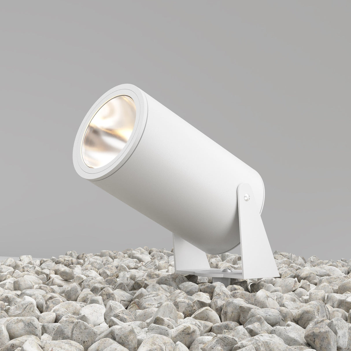 The Bern Outdoor LED Spike Light 30W 3000K in white, boasting an IP65 rating for security, is positioned on gray stones and angled upward against a plain gray backdrop.