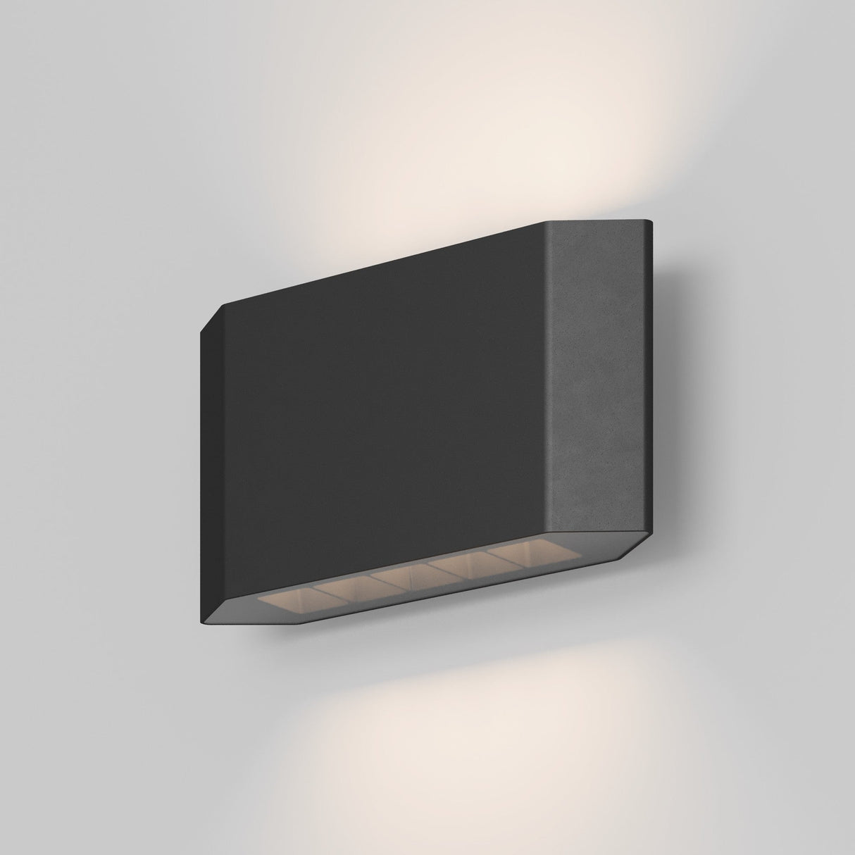 The Pull Outdoor LED Wall Light 8W 3000K in Graphite is a modern, rectangular fixture mounted on a white surface, casting a warm glow with directional lighting as it gently emits from both the top and bottom.