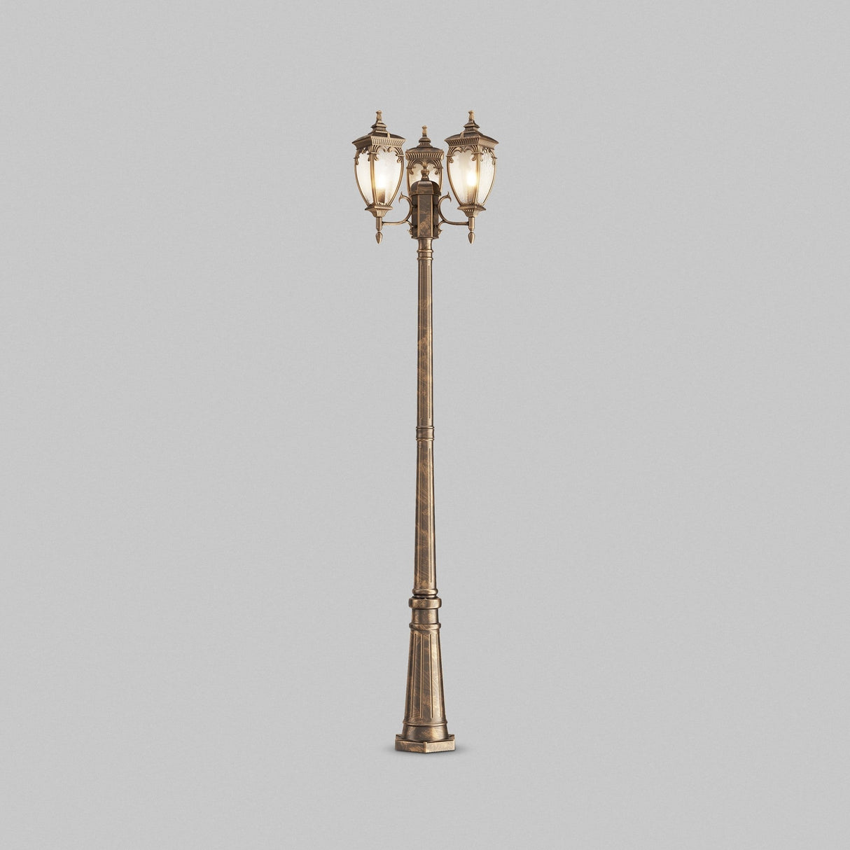 The Fleur 3 Light Triple Head Lamp Post features a tall, ornate design in gold and black. It is crafted from corrosion-resistant aluminum, adorned with three lanterns topped with decorative finials, and set against a plain gray background.