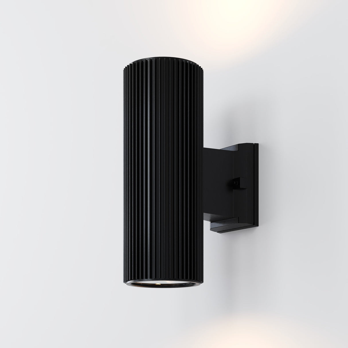 The Rando Outdoor Up & Down Wall Light - Black features a vertical ribbed cylindrical design in matte black, mounted on a light gray wall. It elegantly casts subtle up-and-down lighting for a soft, ambient glow.