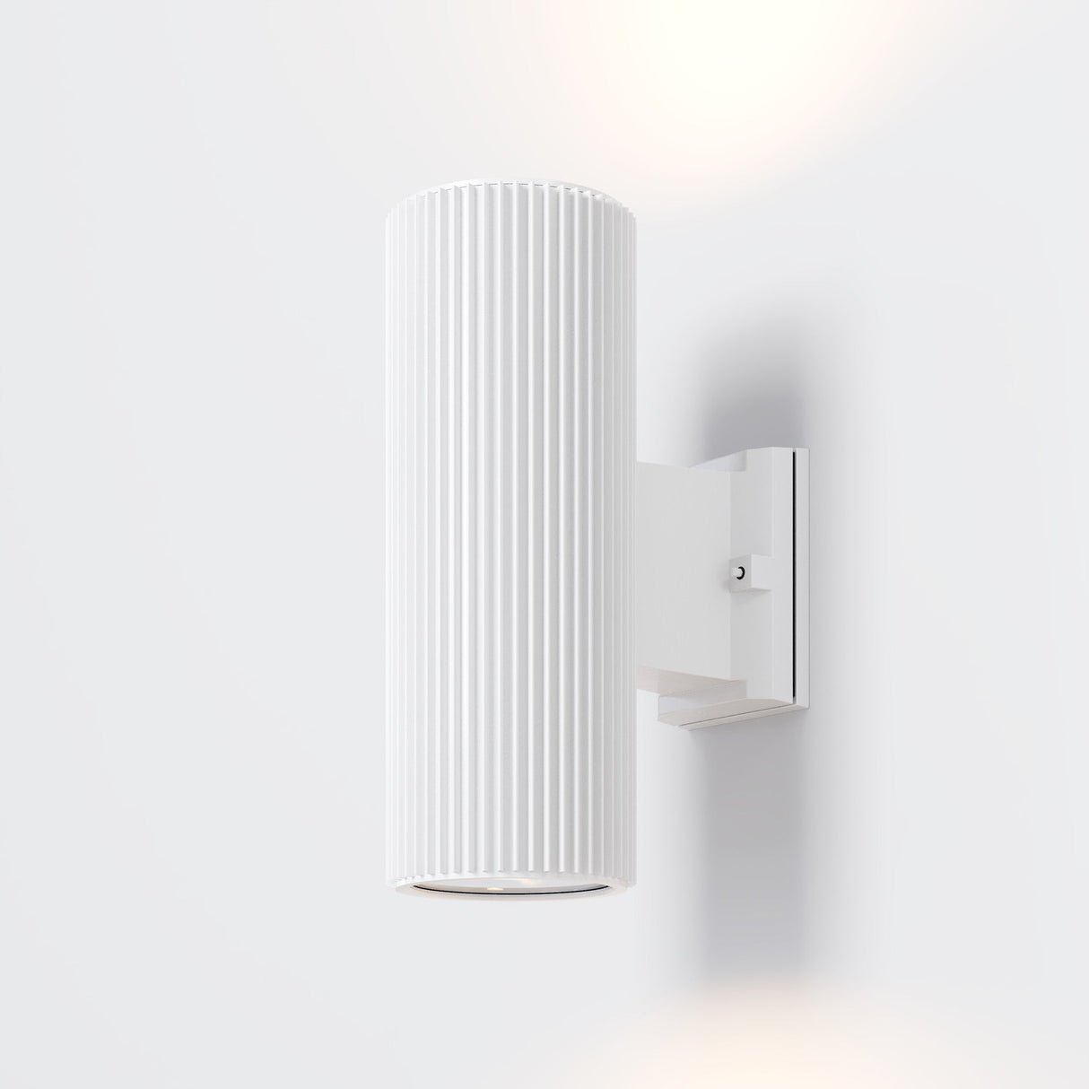 The Rando Outdoor Up & Down Wall Light - White is a cylindrical fixture with vertical grooves, mounted on a square bracket. It provides corrosion-resistant illumination, casting a soft glow above and below on the white wall.