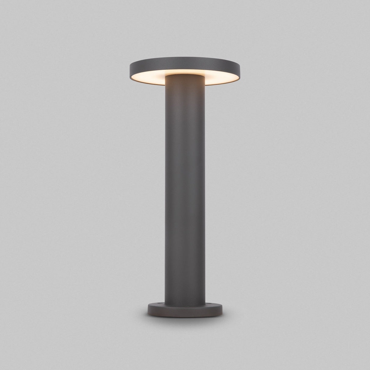 The Wald LED Bollard Light 3000K 12W features a modern cylindrical design, stands at 40cm, boasts a graphite finish and emits soft light from the circular top against a light gray background.