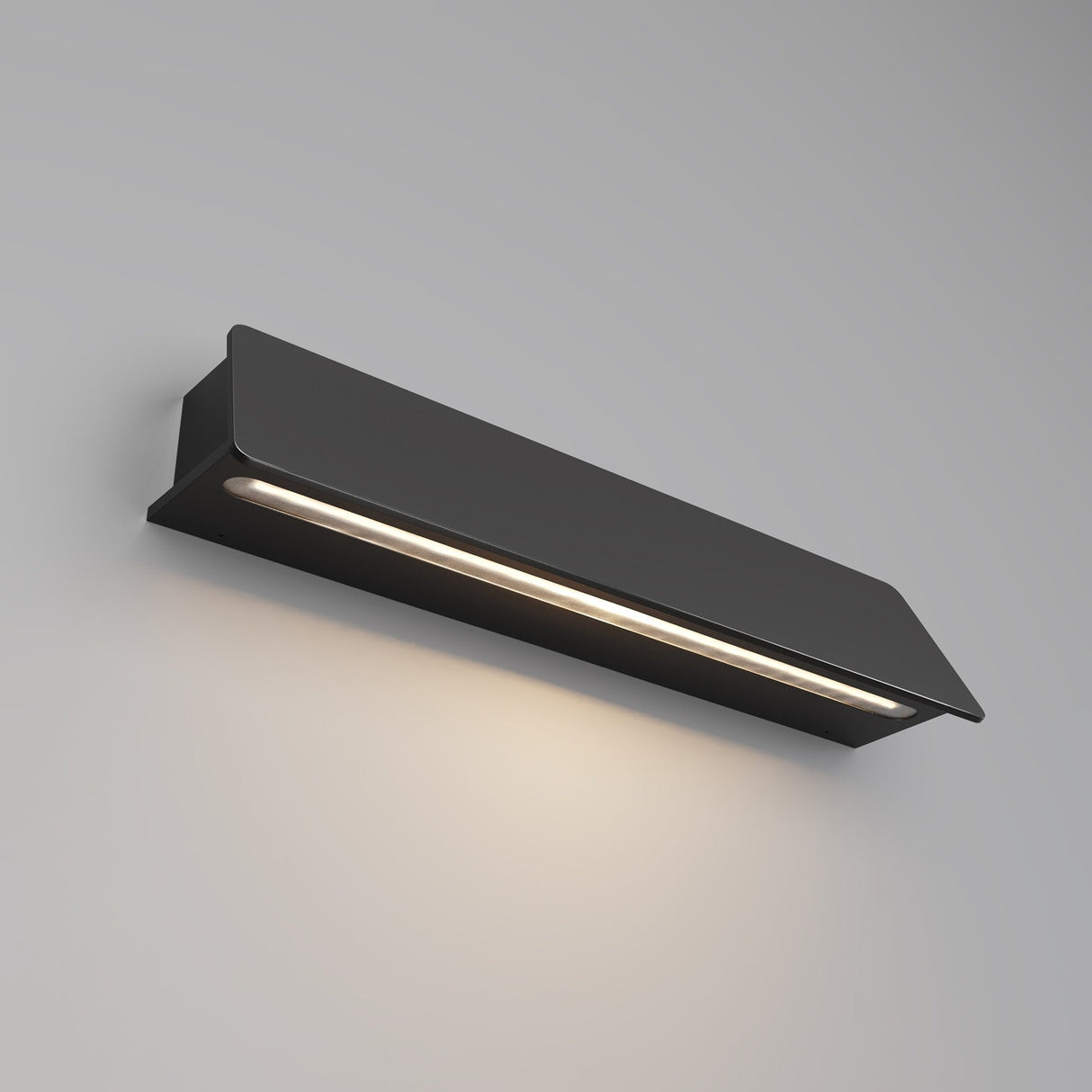 The Trupp Outdoor Wall Light 10W 3000K in a sleek graphite finish mounts on a light gray wall, emitting a soft, warm glow from its narrow horizontal opening and creating a subtle ambiance below.