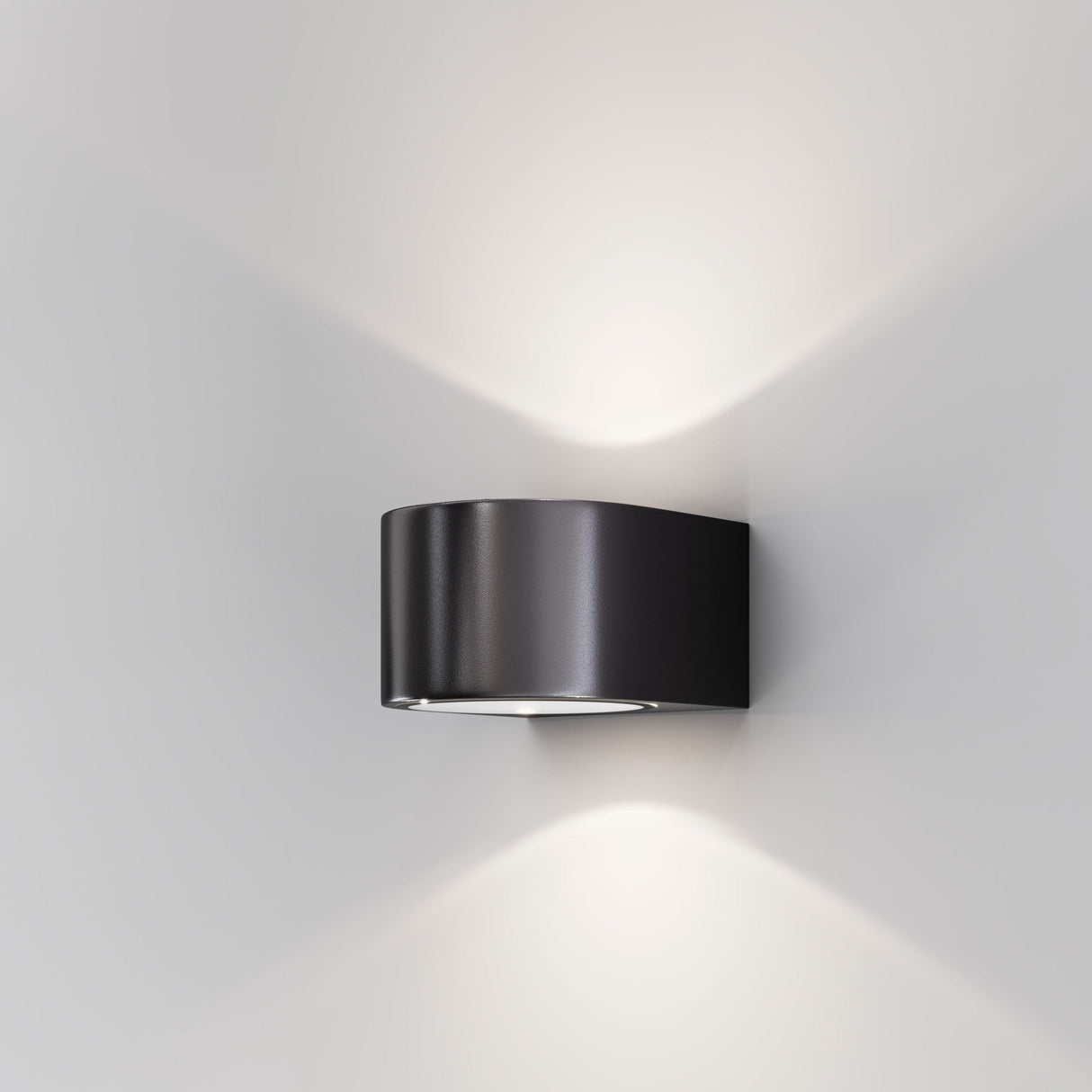 The Blow Outdoor LED Up and Down Wall Light in graphite is installed on a white wall. Rated IP54, this modern fixture provides soft white illumination both upwards and downwards, achieving an elegant minimalist effect.