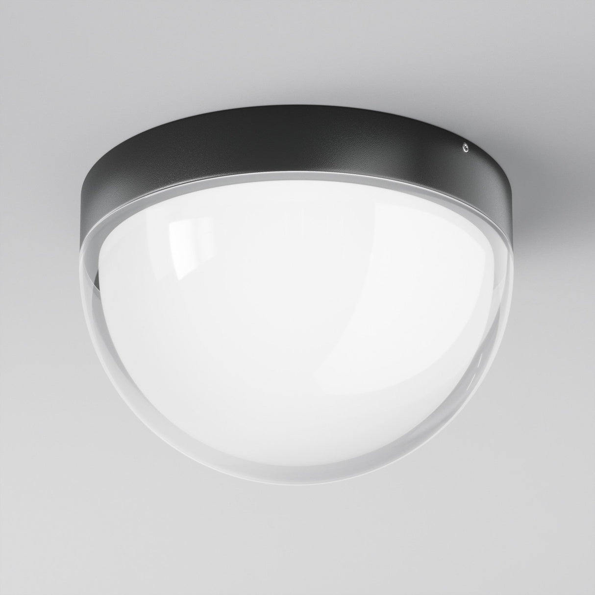 The Mon Outdoor LED Ceiling Light 3000K in Graphite features a modern round design with a graphite metal rim and smooth white glass cover on a white ceiling, offering bright and evenly diffused illumination.