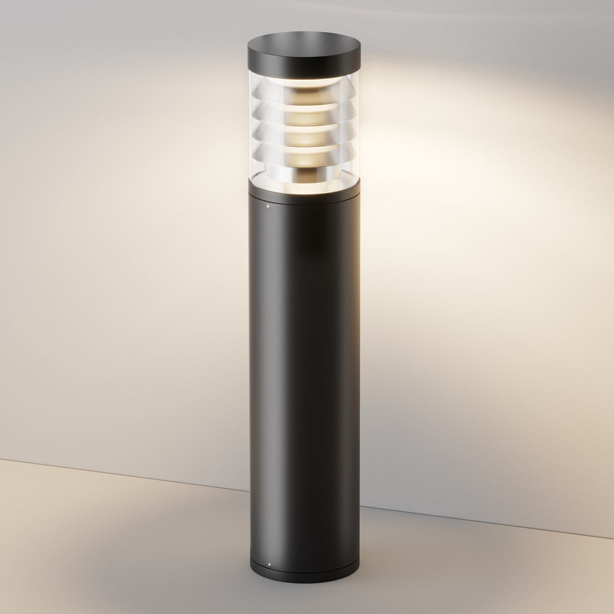 The Spir Bollard Light 3000K 12W - Graphite has a sleek cylindrical black base and a ribbed, translucent top in a graphite finish, emitting a soft, warm glow that enhances any outdoor space with its modern design.