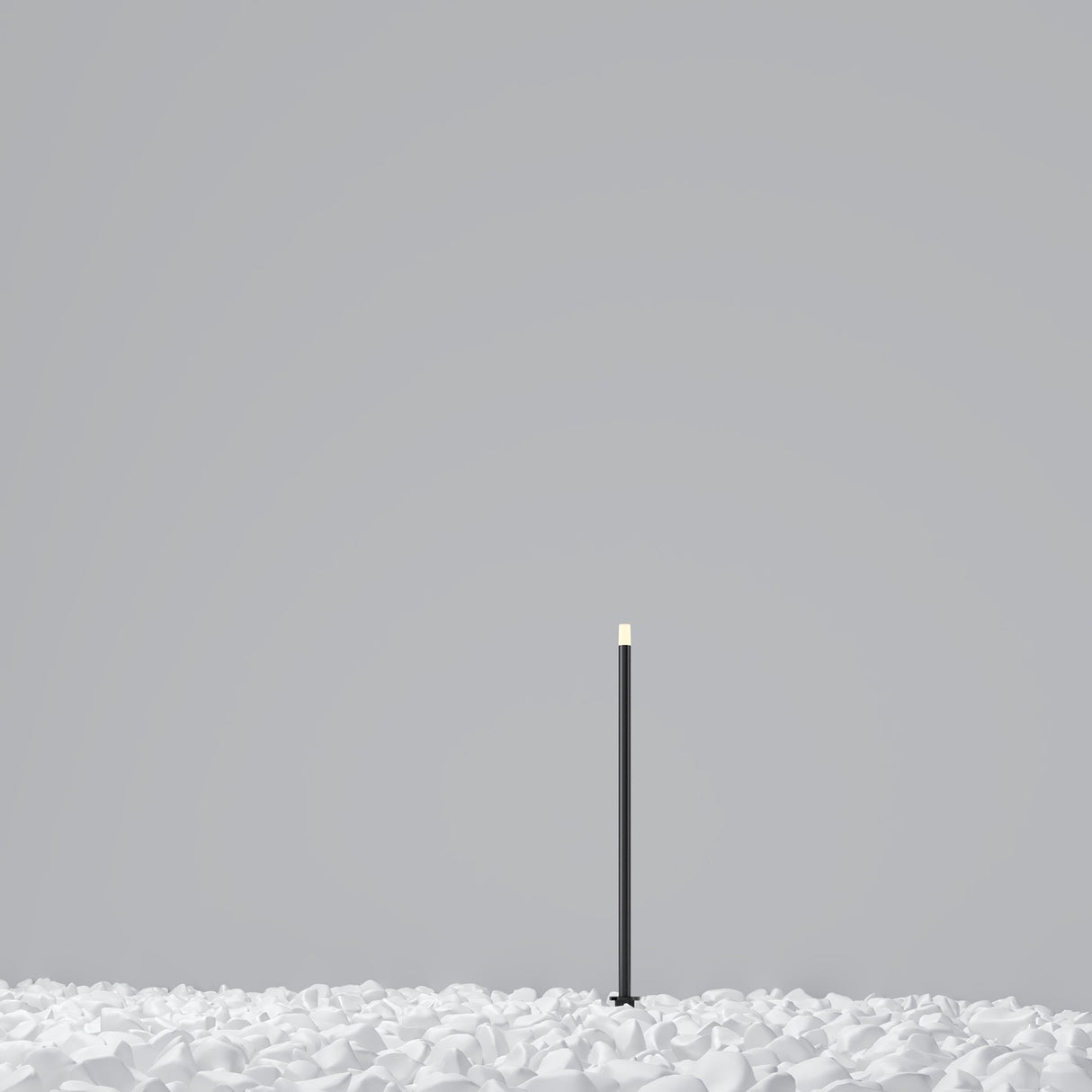 A minimalist image features a tall, slender graphite pole with a small light at the top, like the Spear Outdoor Small Spike Light 3000K 1W. The pole stands on a white surface of petal-like or crumpled paper design against a plain gray background, showcasing its IP65 weather resistance.