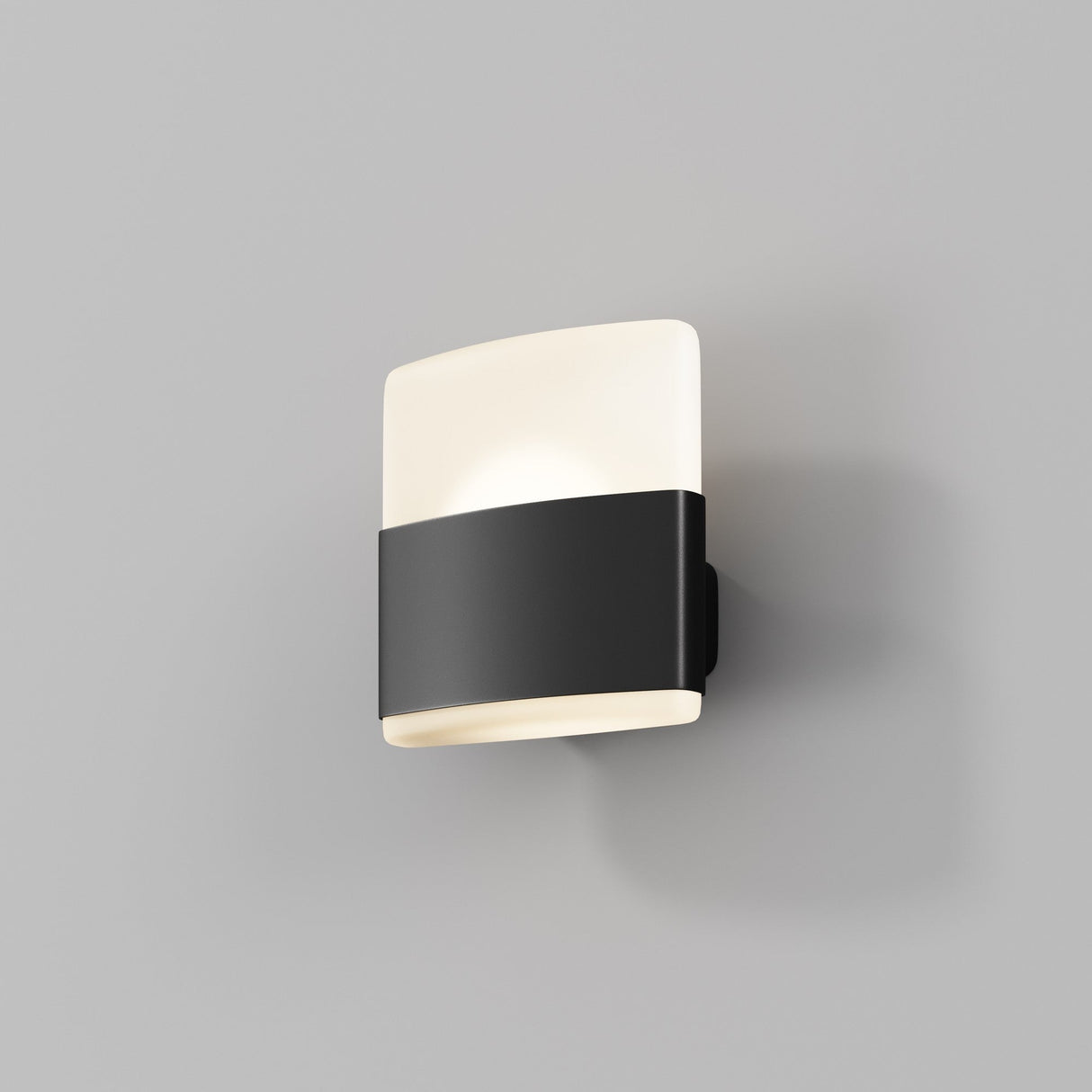The Rom Outdoor LED Wall Light - Graphite is a modern wall-mounted fixture with a minimalist design, featuring a white rectangular shade and an aluminum body. It includes a contrasting black band, casting an energy-efficient glow on the light gray wall.
