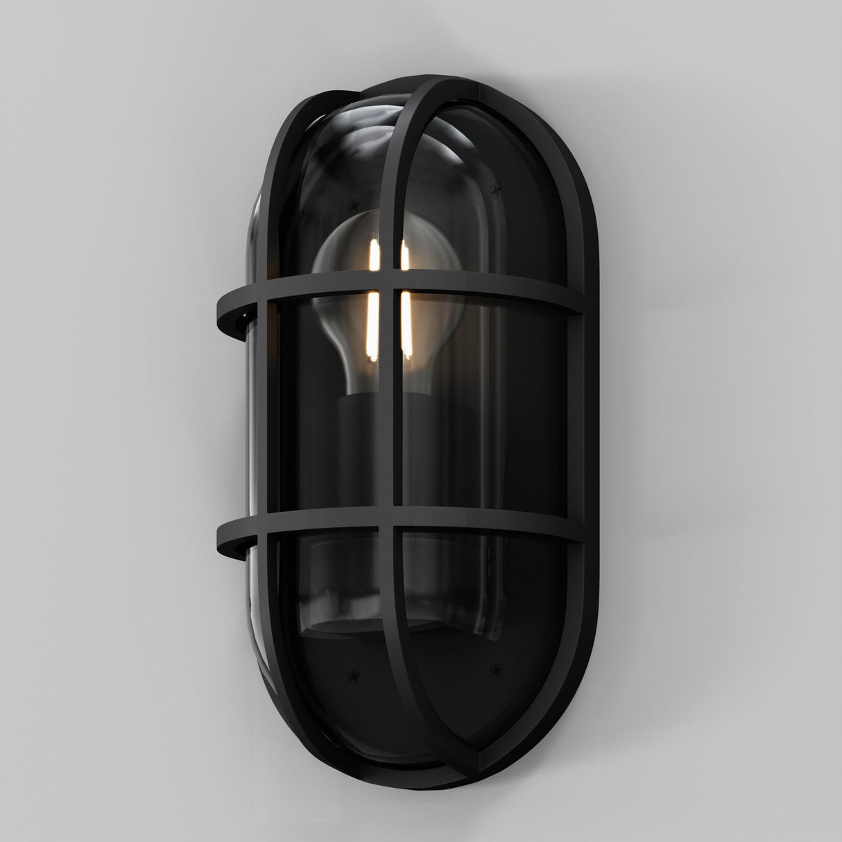 The Candle Outdoor Wall Light in graphite features an industrial-style design with a metal grid and clear glass cover, showcasing the light bulb. This oval fixture, mounted on a plain gray wall, offers a modern industrial look with IP65-rated durability.