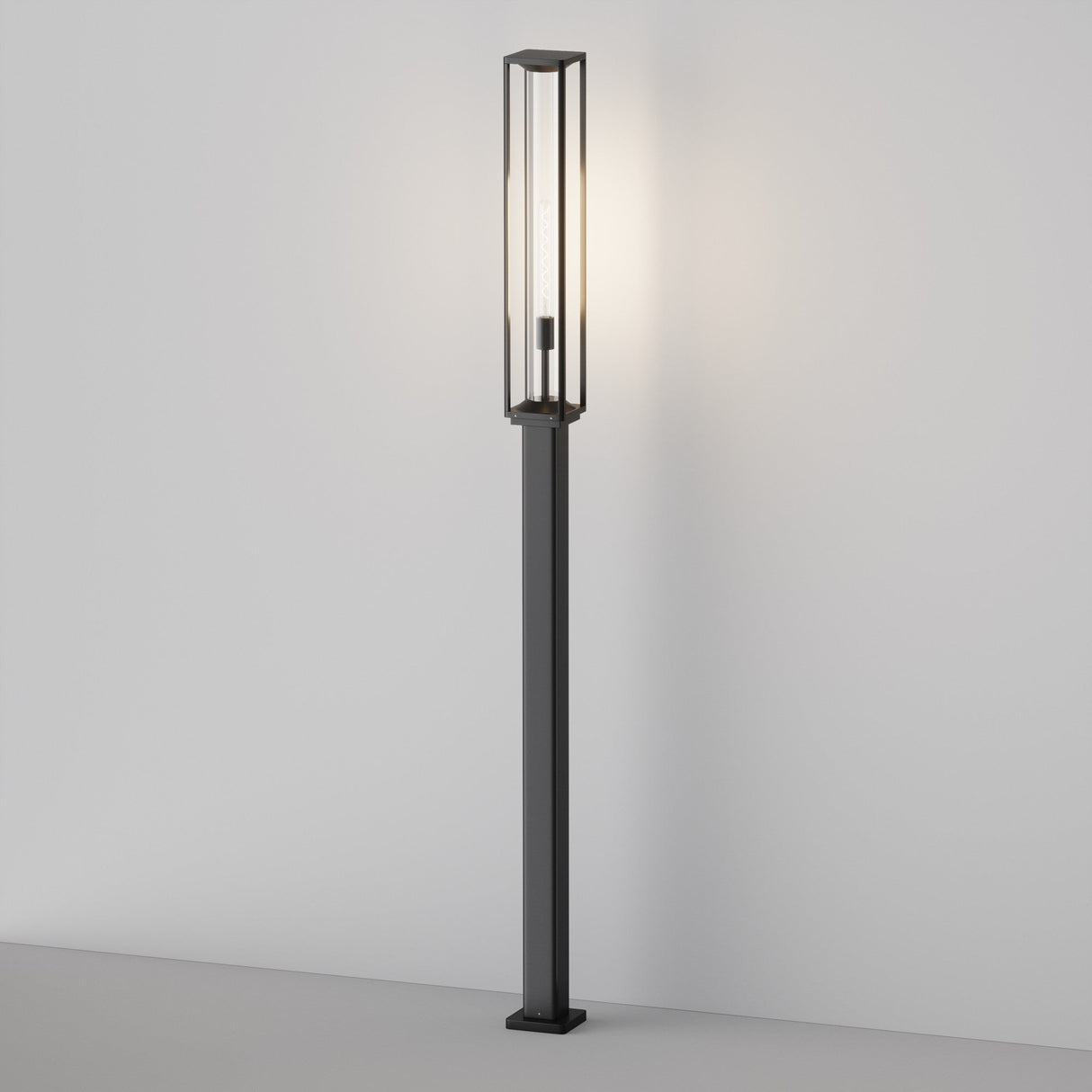 The Cell Bollard Light 220cm - Graphite features a tall, slim frame with a rectangular glass enclosure for soft ambient lighting. Placed against a stark white wall on a light surface, it perfectly captures modern minimalist design akin to sleek outdoor lighting.