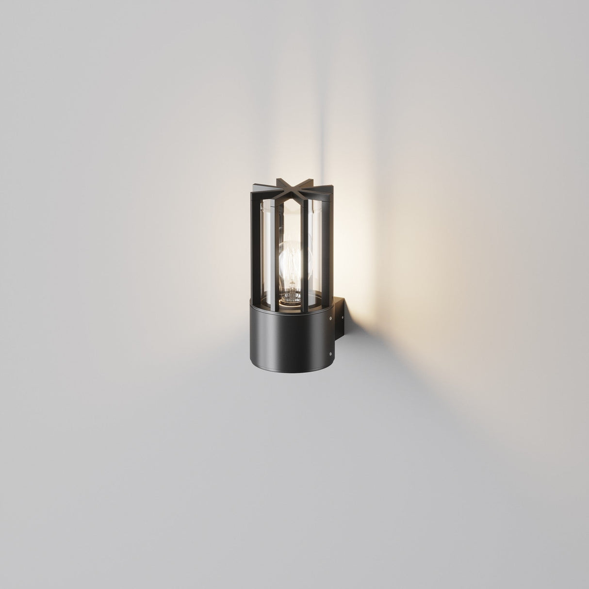 The Barrel Outdoor Wall Light - Graphite is a modern black wall sconce with an industrial design and cylindrical shape, showcasing a visible bulb. Mounted on a light gray wall, its graphite finish adds sophistication while the bulb softly illuminates the surface behind.