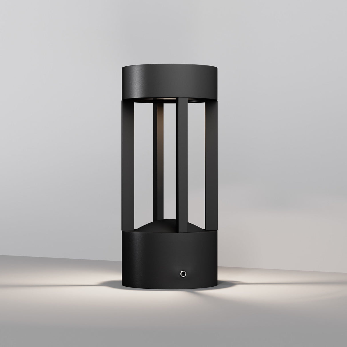 The Vint LED Outdoor Wall Light (3000K 9W, Graphite, 20cm) is sleek and modern, featuring a cylindrical design with vertical slats and a hollow center. Its IP65 rating ensures soft illumination from its base on a light gray surface, enhancing the surrounding ambiance.