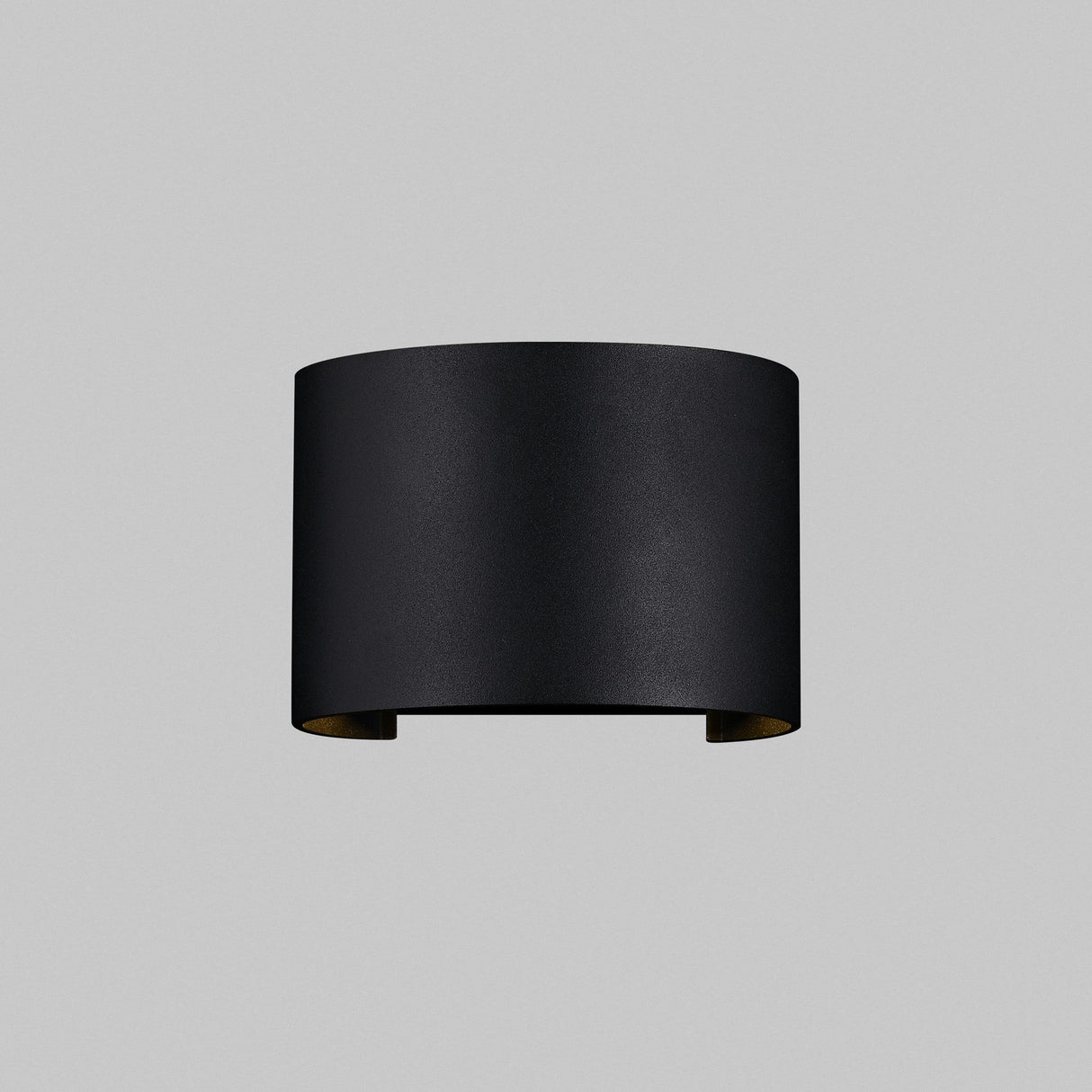 The Fulton Outdoor LED Oval Wall Light - Black features a minimalist, cylindrical design with an open top and bottom, made from corrosion-resistant aluminum, and mounted on a plain gray background.