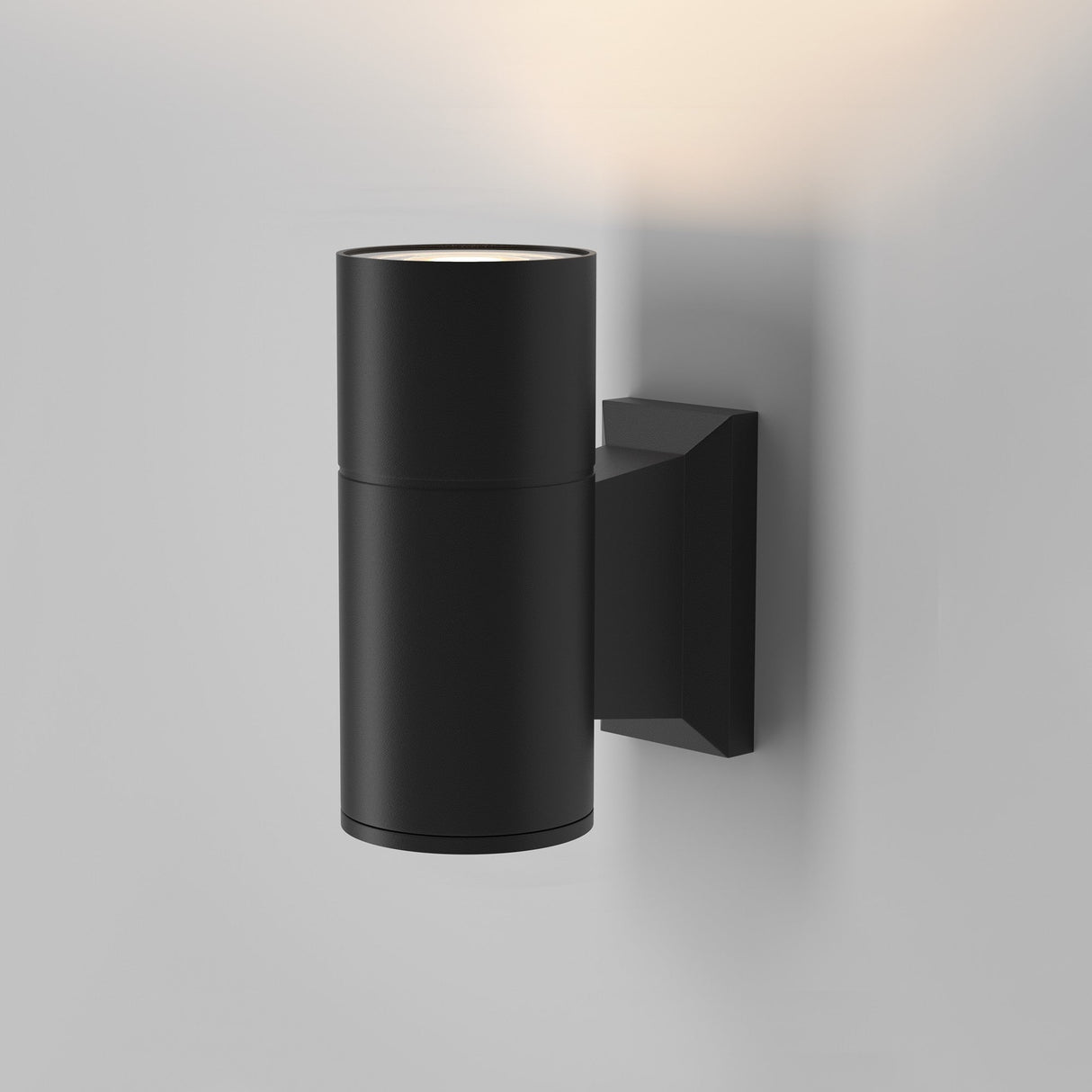 The Bowery Outdoor 1 Light Wall Light - Black (O574WL-01B) offers a minimalist design with a sleek black cylindrical shape, IP54 rating, and upward/downward beams attached to a rectangular base on a plain white wall.