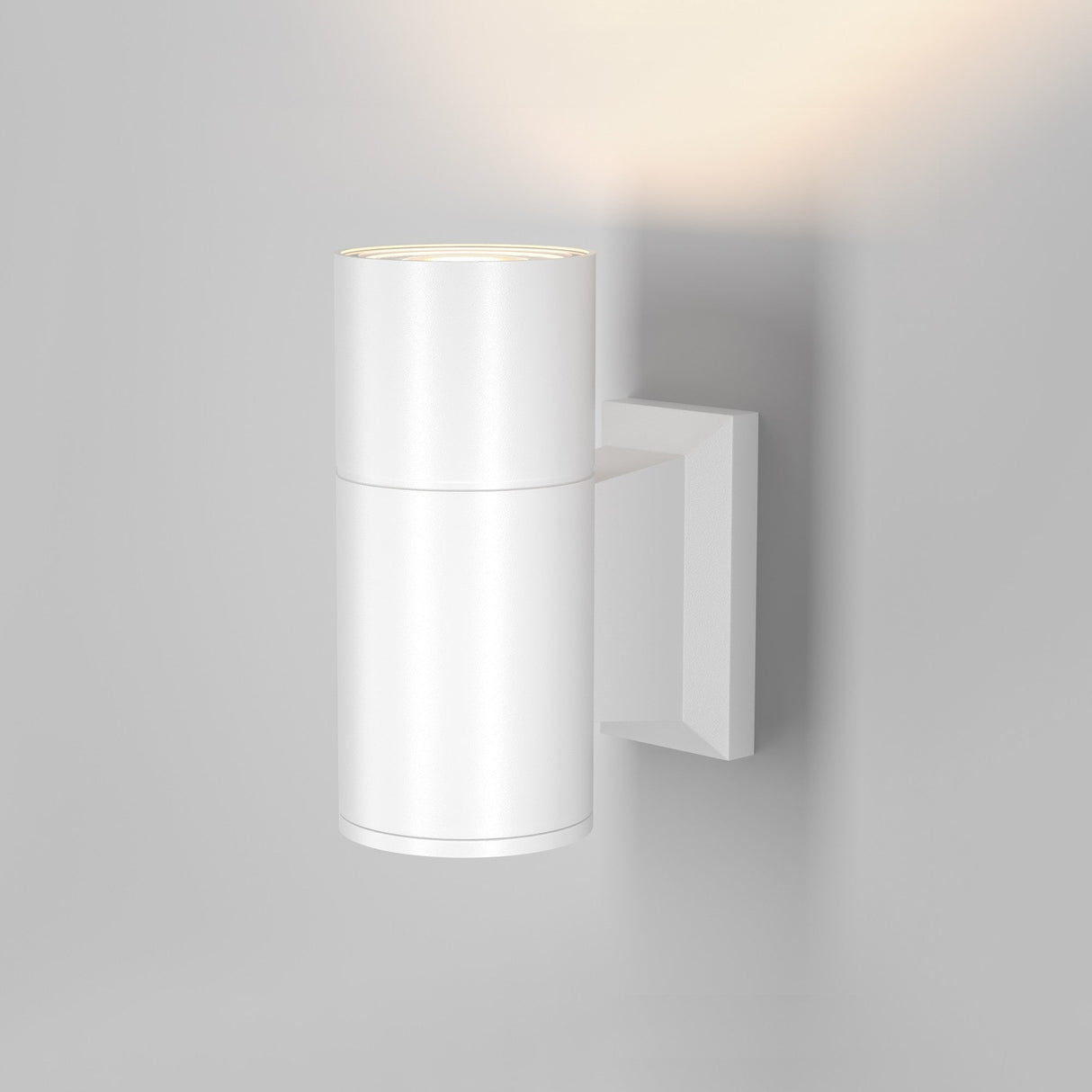 The Bowery Outdoor 1 Light Wall Light - White (O574WL-01W) with a modern, cylindrical, weather-resistant design is mounted on a plain white wall. It emits a soft upward glow.