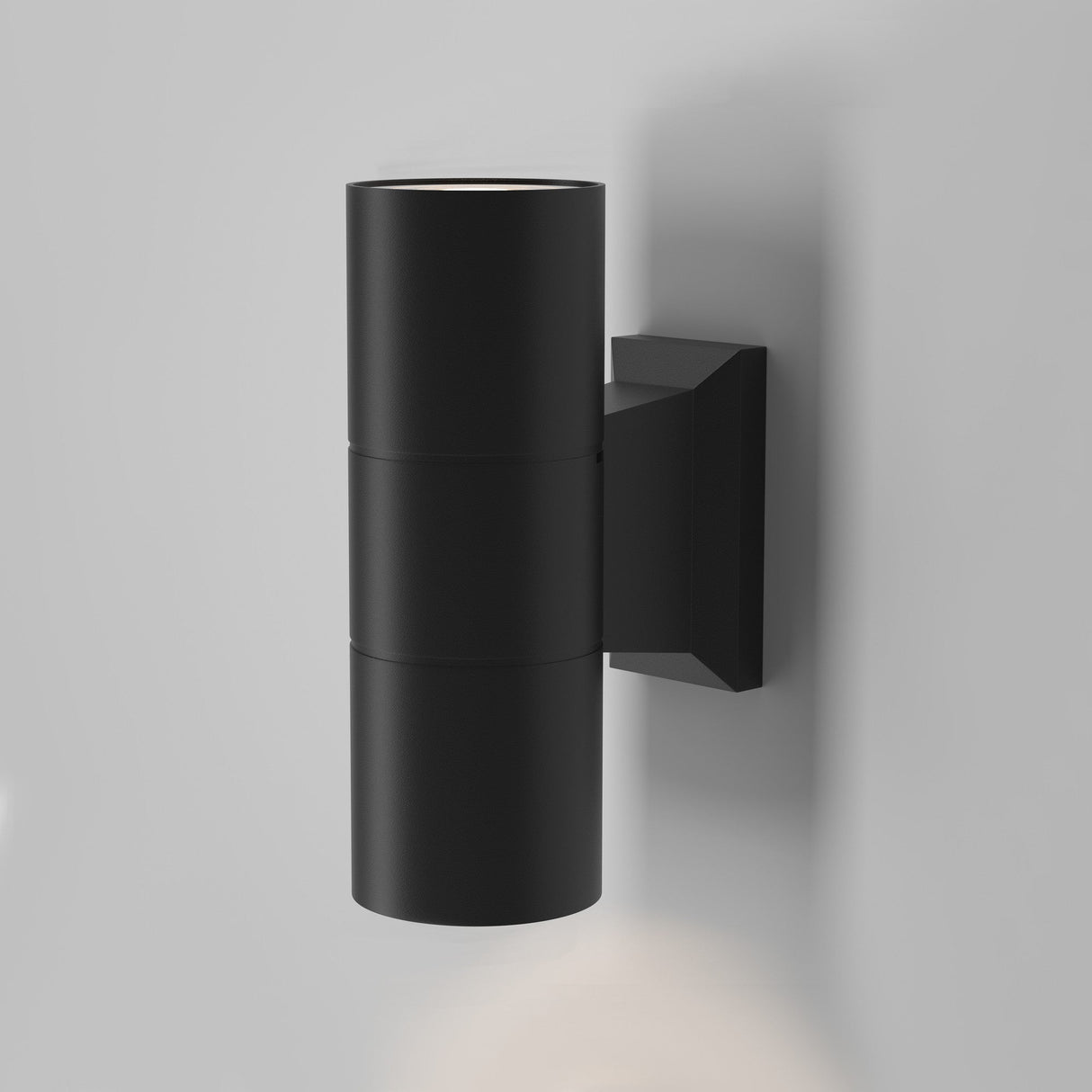 The Bowery Outdoor 2 Light Wall Light - Black (O574WL-02B) is a modern cylindrical wall sconce on a light gray wall, offering an up-and-down light design. Sleek and minimalist, it emits soft glows from both ends and is IP54 rated for durability and elegance.