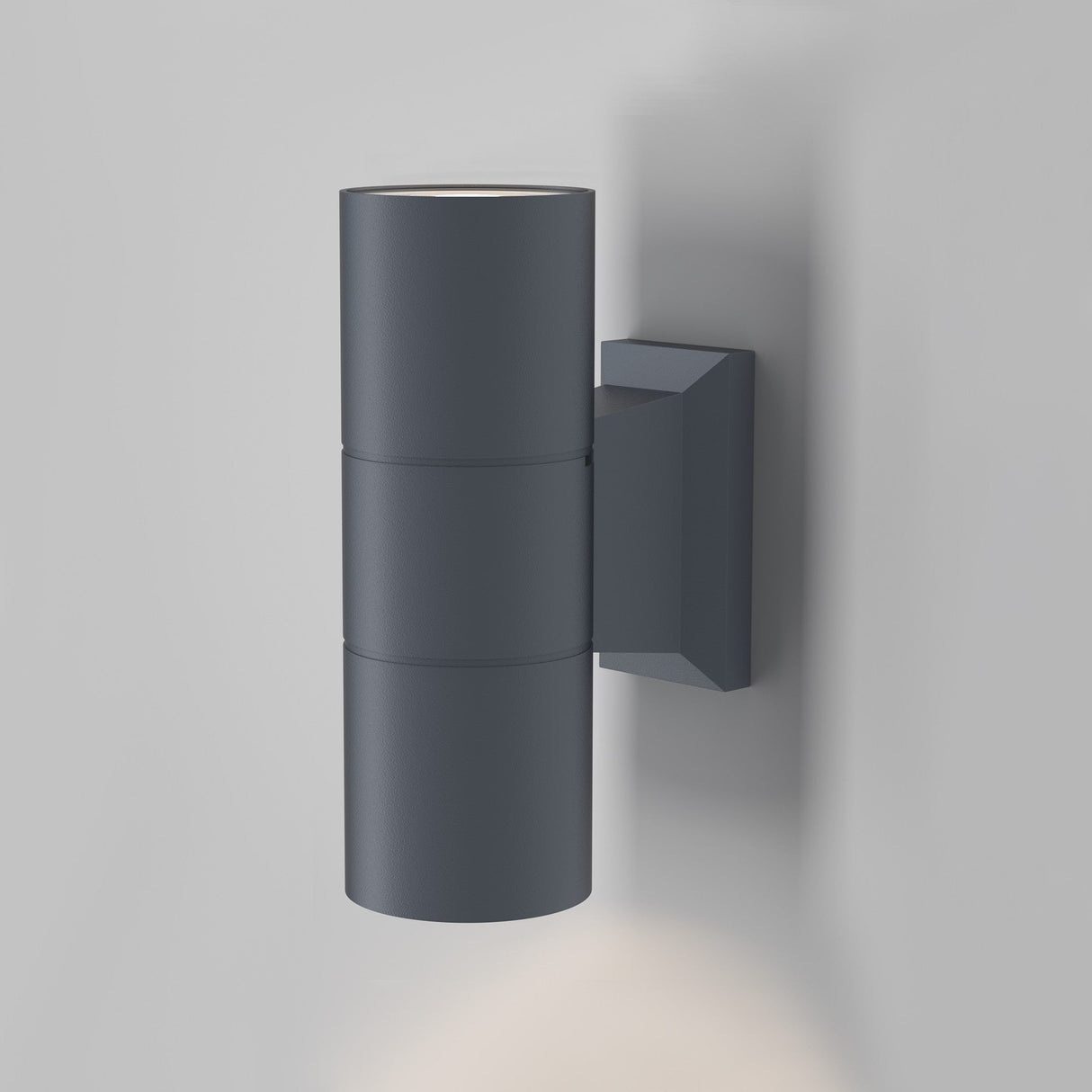 The Bowery Outdoor 2 Light Wall Light (O574WL-02GR) is a contemporary wall fixture with a cylindrical shape and square base in matte grey. It offers bidirectional illumination, casting light both upward and downward.