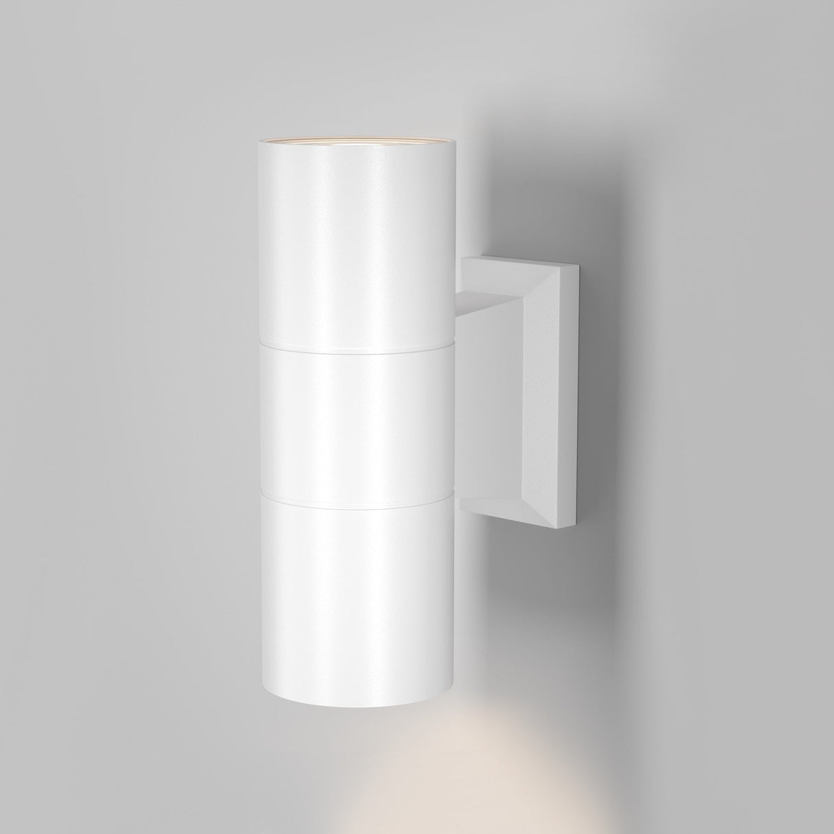 The Bowery Outdoor 2 Light Wall Light - White (O574WL-02W) is a modern cylindrical white sconce on a light gray wall, offering dual light output with a minimalist design, illuminating both upward and downward.