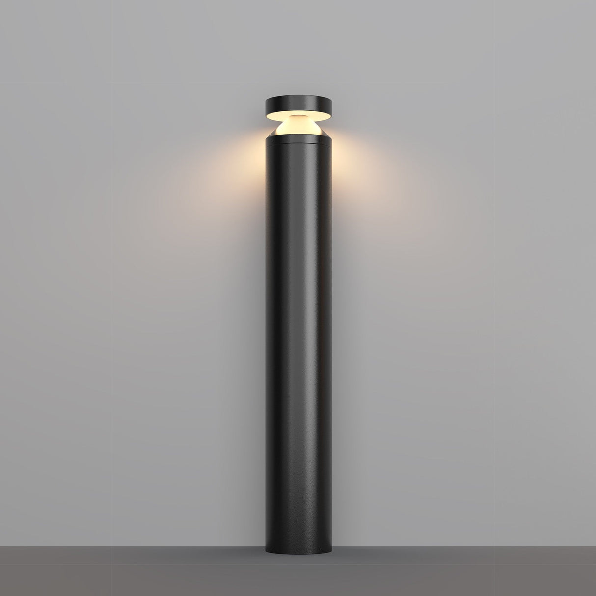 The minimalist Olten Bollard Light 80cm in Graphite, with its cylindrical base and round top, emits a soft, warm LED glow onto the light gray wall.
