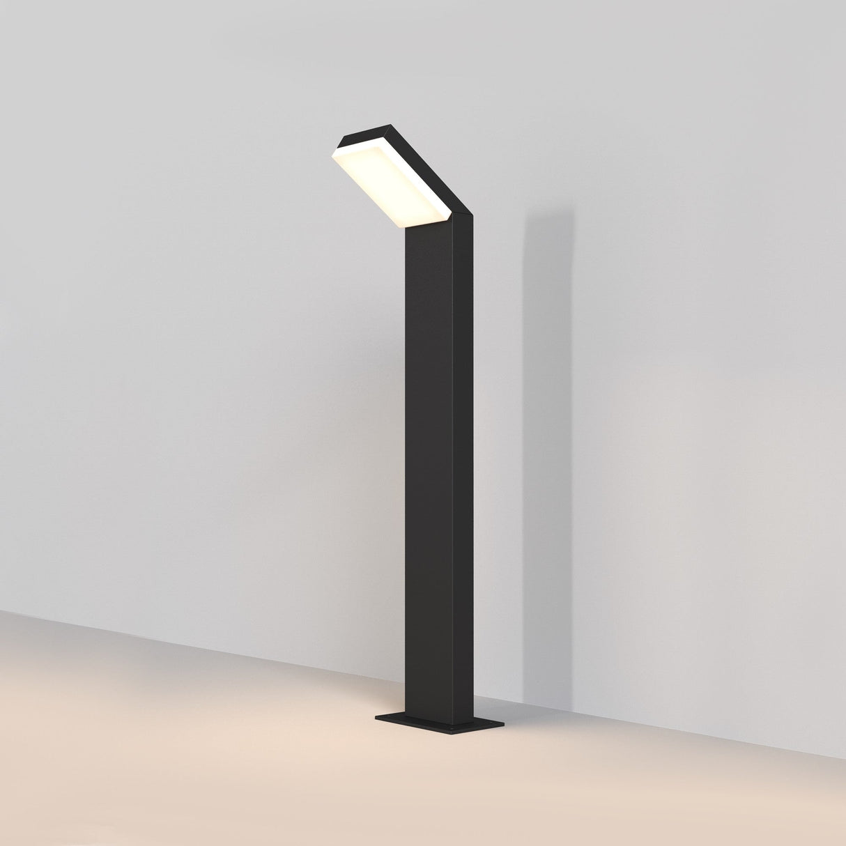 The Paso LED Bollard Light 80cm in black is a sleek, modern floor lamp featuring a tall rectangular base and a slightly angled fixture, illuminating with an energy-efficient soft white light that casts a subtle shadow against a white wall.