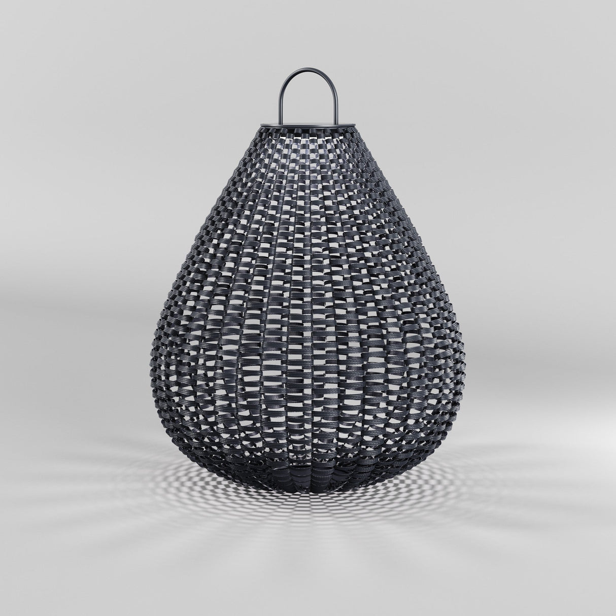 The Plet Pedestal Light 61cm- Black is a teardrop-shaped rattan lantern on a light gray surface. Its intricate design casts delicate shadows and includes a small top handle. Ideal for outdoor lighting, it features an eco-friendly solar battery.