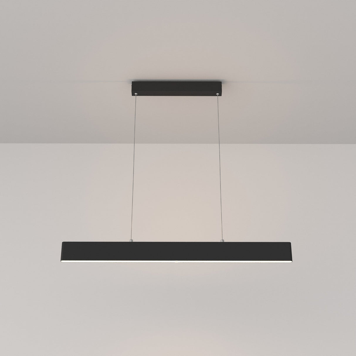 The Step LED Linear Suspension Light 3000K 23W in black, featuring minimalist design and advanced SMD LED technology, hangs from the ceiling by two thin wires, casting a soft glow on the plain white ceiling and wall.