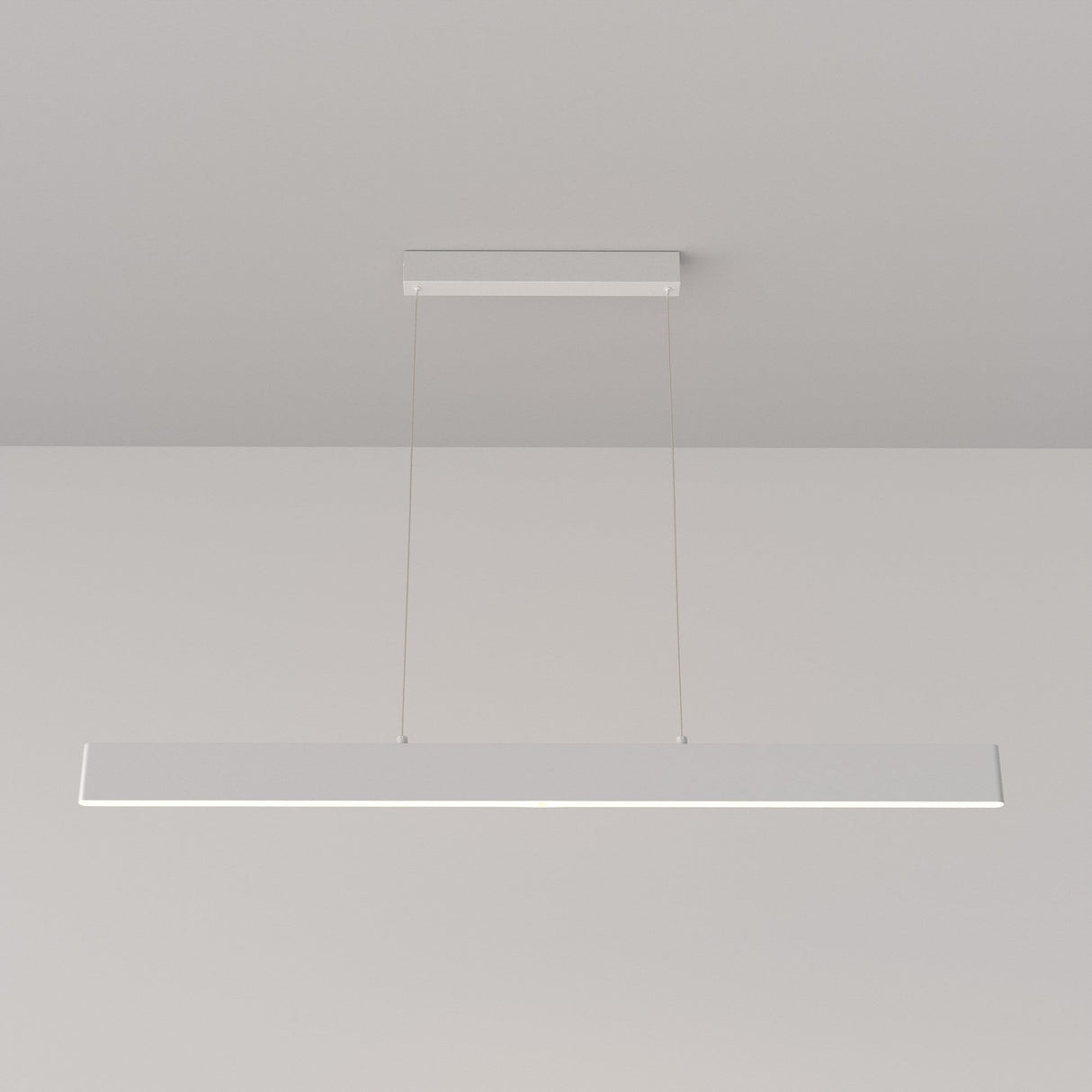 The Step LED Long Linear Suspension Light 3000K 30W - White, with its minimalist and modern design, hangs from the ceiling by two thin wires against a plain white backdrop. It features advanced SMD LED technology for efficient illumination.