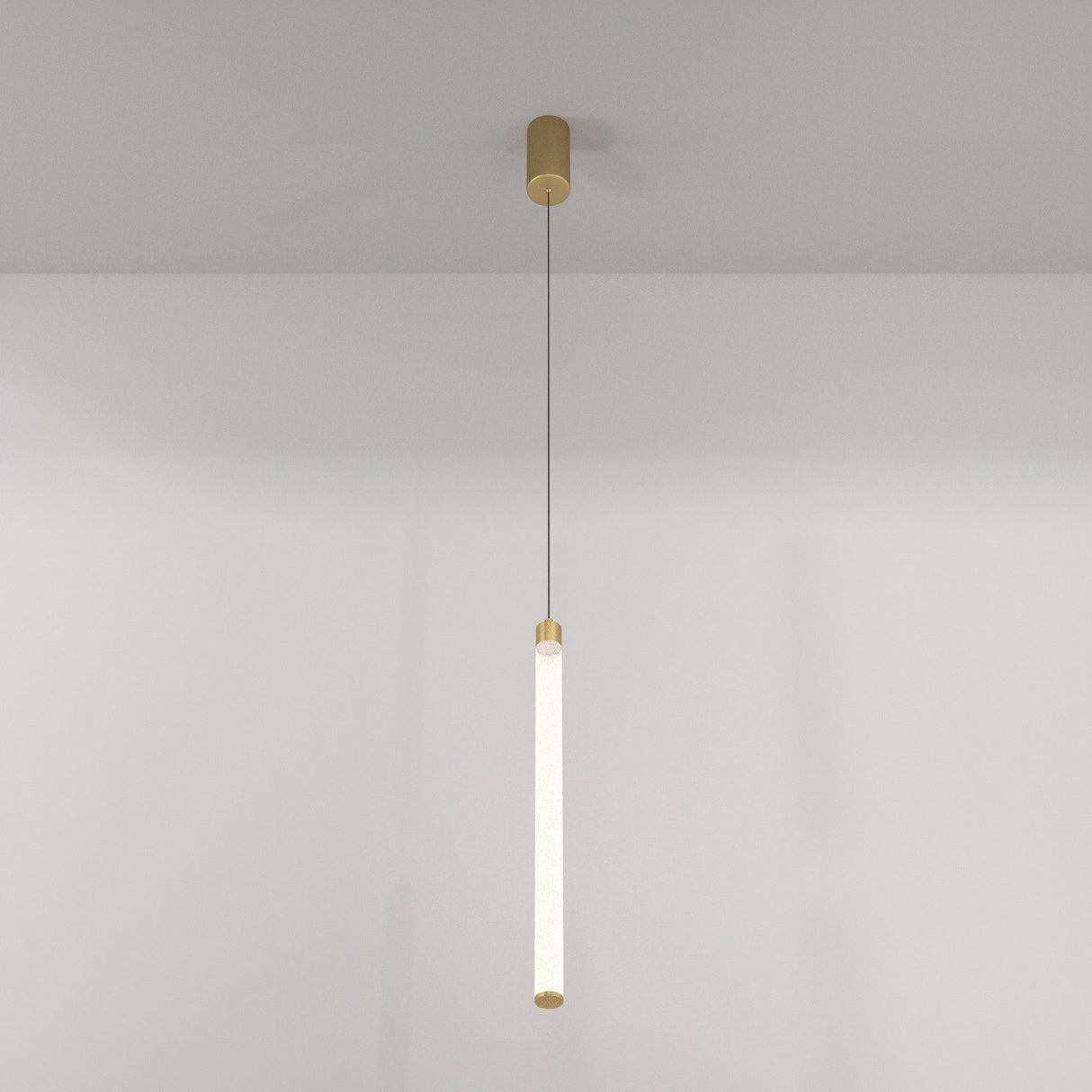 The Ray LED Long Pendant Light - Gold & White hangs by a thin cord, featuring a cylindrical beige mount and frosted tubular light fixture with matte gold accents. It complements the plain, light-colored wall with its minimalist design.