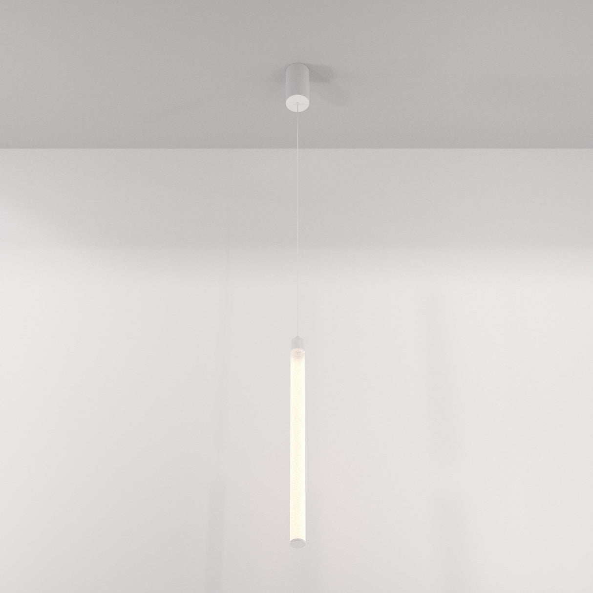 The Ray LED Long Pendant Light - White elegantly hangs from the ceiling with a minimalist cylindrical design and thin cable against a plain white backdrop, ideal for contemporary interiors and providing soft illumination that enhances modern spaces.