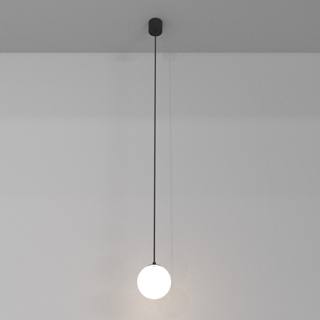 The Luna LED Globe Pendant Light 10cm 4000K - Black & White features a glowing white sphere that complements modern interiors. Suspended from a black cord against a gray ceiling, it offers energy-efficient lighting, enhancing simplicity and elegance against its plain white backdrop.