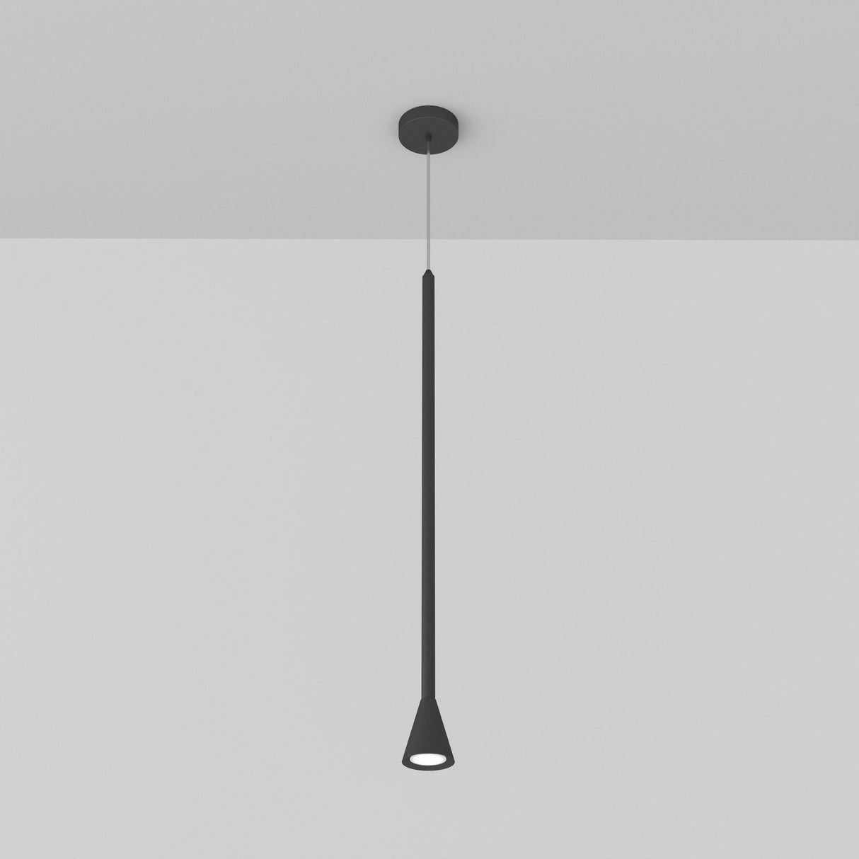 The Arrow 1 Light Long Cone Pendant in black features a minimalist design with an elongated, conical shape. It hangs from a white ceiling, emitting a subtle glow and adjustable in height for versatile placement.